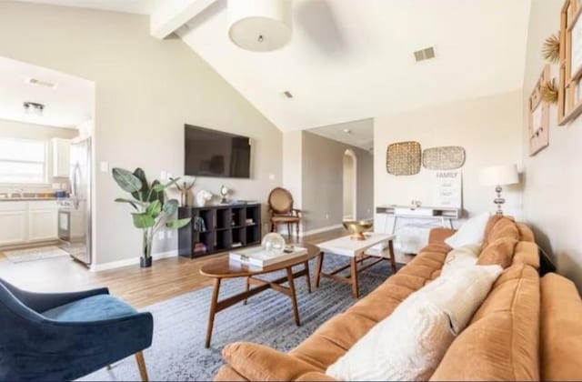 living room featuring beamed ceiling, light wood-type flooring, high vaulted ceiling, and ceiling fan