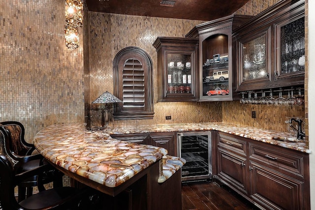 bar featuring light stone counters, dark brown cabinetry, sink, and wine cooler