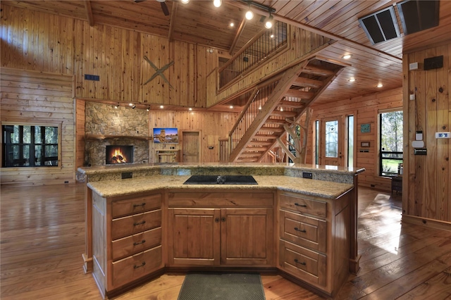 kitchen featuring black electric stovetop, wood ceiling, wooden walls, and light hardwood / wood-style flooring