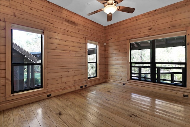 unfurnished room with wood walls, light hardwood / wood-style flooring, and ceiling fan