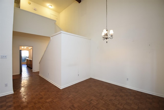 spare room with a chandelier, dark parquet floors, and high vaulted ceiling