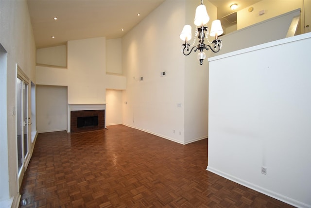 unfurnished living room with dark parquet floors, a fireplace, a high ceiling, and a chandelier