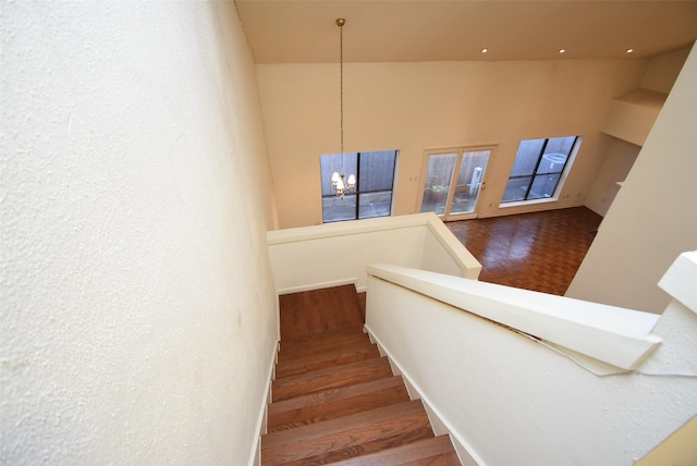 stairway featuring wood-type flooring, an inviting chandelier, and high vaulted ceiling