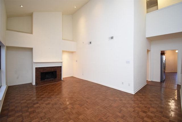 unfurnished living room with dark parquet flooring, a fireplace, and a towering ceiling