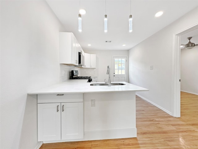 kitchen with white cabinetry, hanging light fixtures, black range oven, and sink