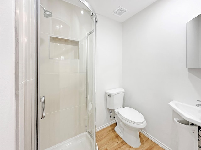 bathroom with hardwood / wood-style floors, toilet, and a shower with shower door