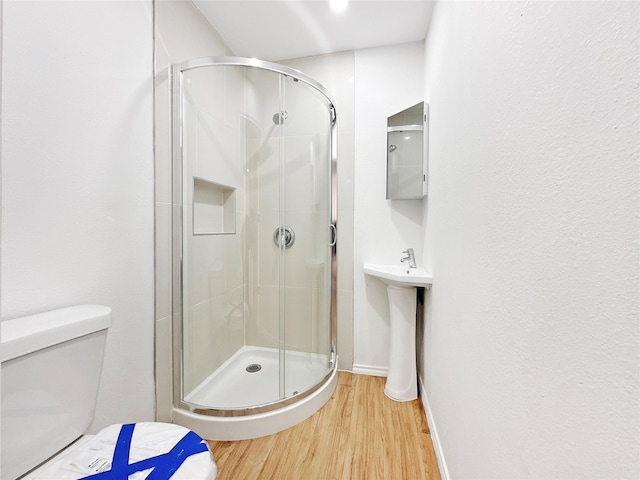 bathroom featuring wood-type flooring, toilet, a shower with shower door, and sink