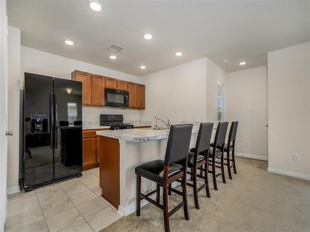 kitchen with sink, light colored carpet, a kitchen bar, a kitchen island with sink, and black appliances