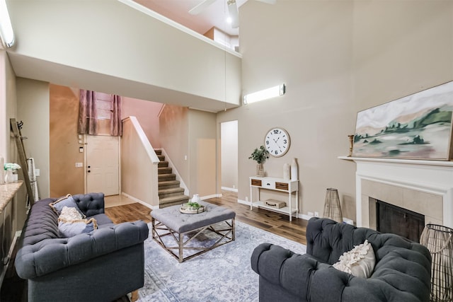 living room featuring ceiling fan, wood-type flooring, a towering ceiling, and a tile fireplace