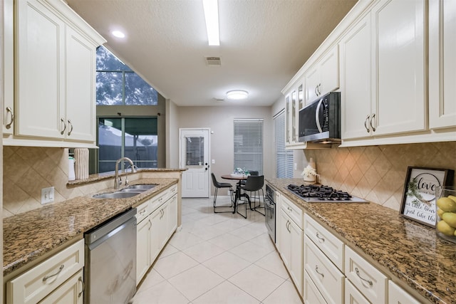 3102 Silver Cedar Trl, Katy, TX 77449 - kitchen featuring stainless steel appliances, a sink, light tile patterned floors, stone countertops, and a textured ceiling