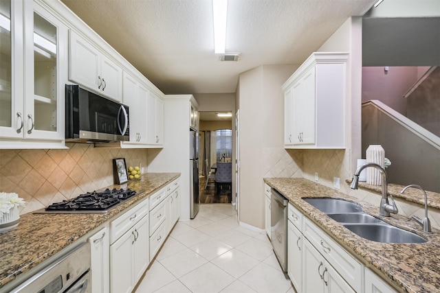 3102 Silver Cedar Trl, Katy, TX 77449 - kitchen featuring appliances with stainless steel finishes, a sink, white cabinetry, glass insert cabinets, and a textured ceiling