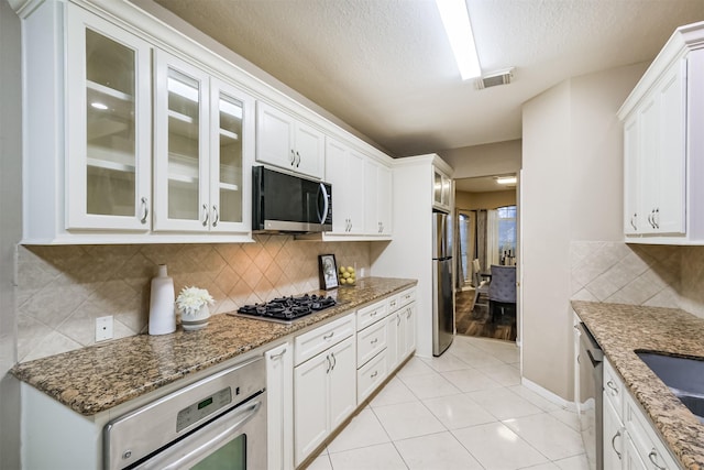 3102 Silver Cedar Trl, Katy, TX 77449 - kitchen featuring stainless steel appliances, glass insert cabinets, white cabinets, light stone counters, and a textured ceiling