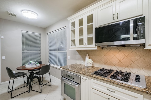 3102 Silver Cedar Trl, Katy, TX 77449 - kitchen featuring appliances with stainless steel finishes, baseboards, tasteful backsplash, light stone countertops, and glass insert cabinets