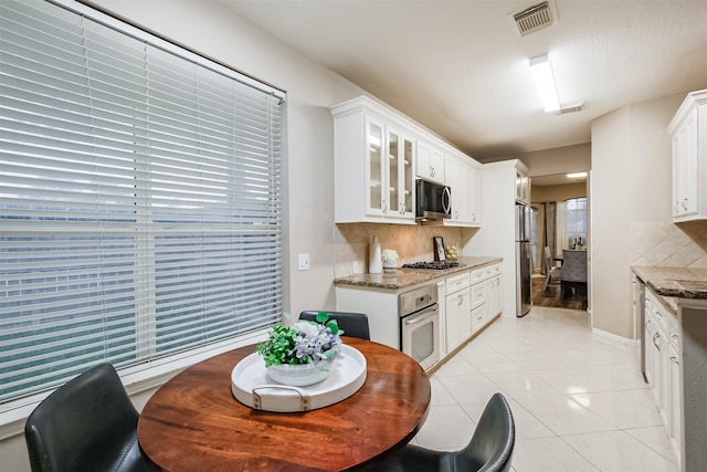 3102 Silver Cedar Trl, Katy, TX 77449 - kitchen featuring appliances with stainless steel finishes, backsplash, light stone countertops, and glass insert cabinets
