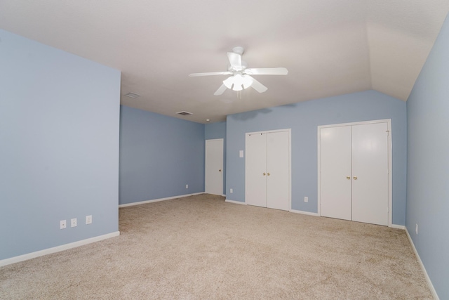 unfurnished bedroom featuring ceiling fan, vaulted ceiling, light carpet, and multiple closets