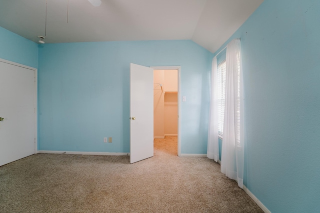 unfurnished bedroom with ceiling fan, vaulted ceiling, a walk in closet, light carpet, and a closet