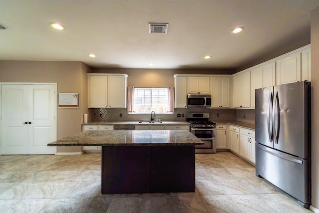 kitchen featuring sink, a center island, dark stone countertops, white cabinets, and appliances with stainless steel finishes