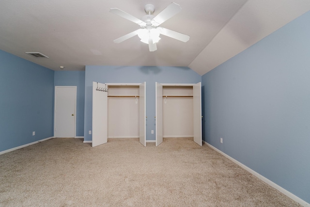 unfurnished bedroom with ceiling fan, vaulted ceiling, light colored carpet, and two closets