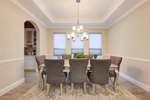 dining space with ornamental molding, a tray ceiling, and an inviting chandelier