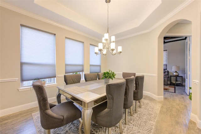 dining space with a tray ceiling, an inviting chandelier, ornamental molding, and light wood-type flooring