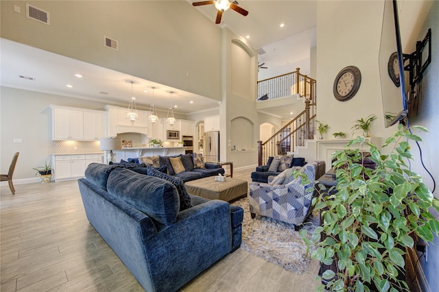 living room with ceiling fan, light hardwood / wood-style flooring, a towering ceiling, and crown molding