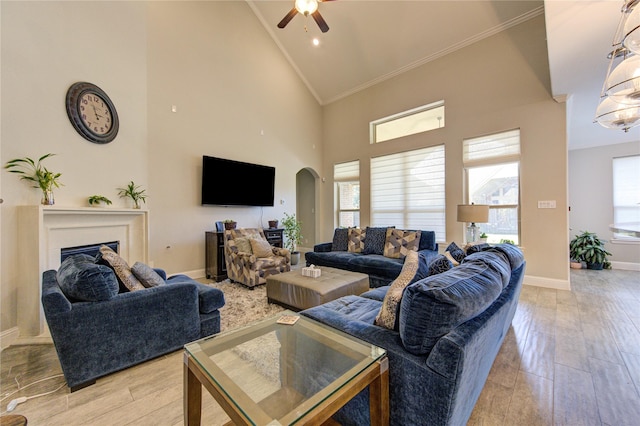 living room with light wood-type flooring, high vaulted ceiling, ceiling fan, and ornamental molding