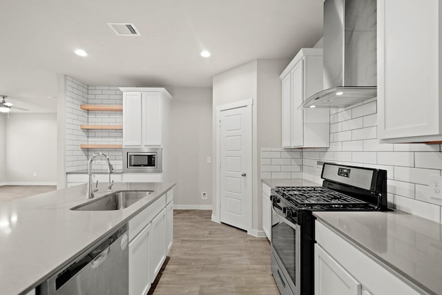 kitchen with white cabinets, wall chimney range hood, sink, light hardwood / wood-style floors, and stainless steel appliances