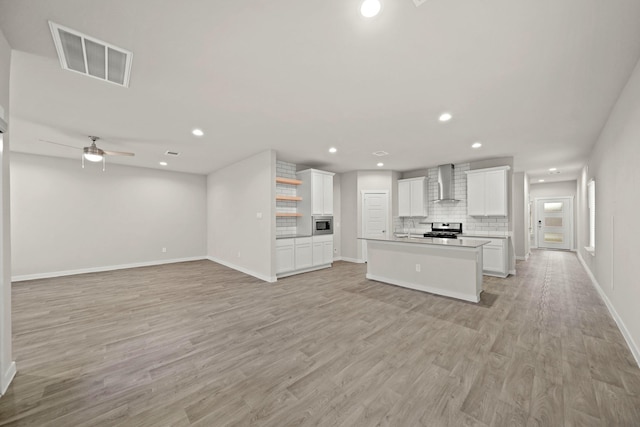 kitchen featuring white cabinetry, wall chimney exhaust hood, stainless steel appliances, light hardwood / wood-style flooring, and an island with sink