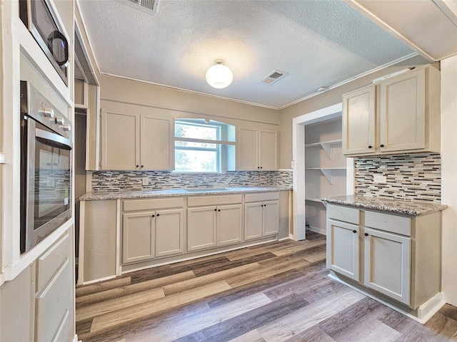 kitchen with stainless steel oven, light wood-type flooring, sink, and tasteful backsplash