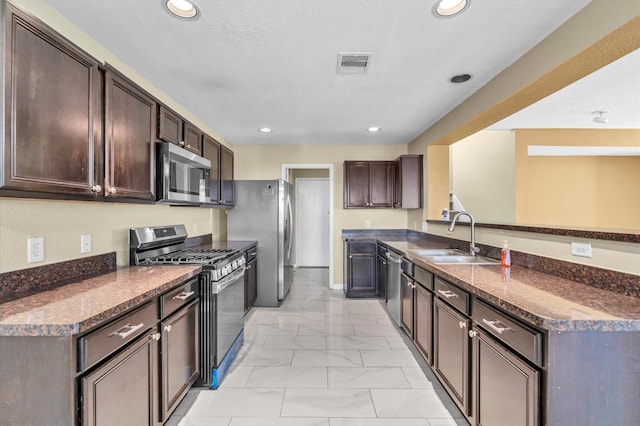 kitchen with sink, stainless steel appliances, dark stone counters, a textured ceiling, and dark brown cabinets