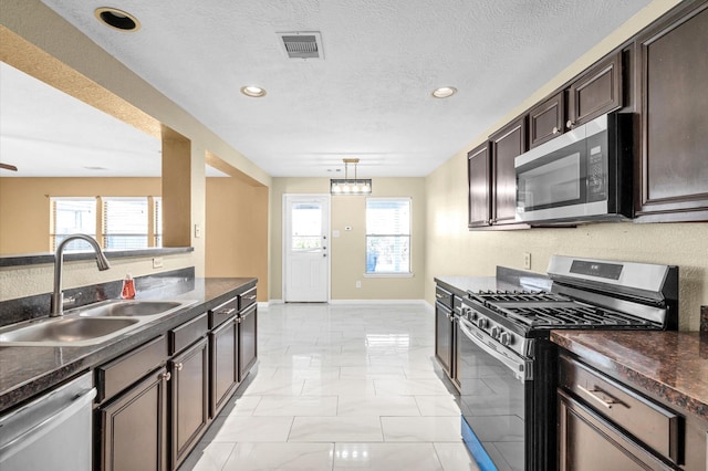 kitchen featuring sink, hanging light fixtures, a textured ceiling, dark brown cabinets, and appliances with stainless steel finishes