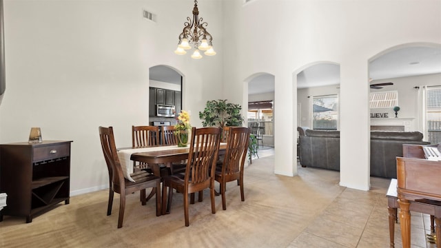 dining space featuring a towering ceiling, light colored carpet, and ceiling fan with notable chandelier