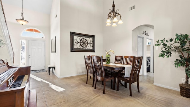 dining room with a chandelier, washer / dryer, a towering ceiling, and light colored carpet