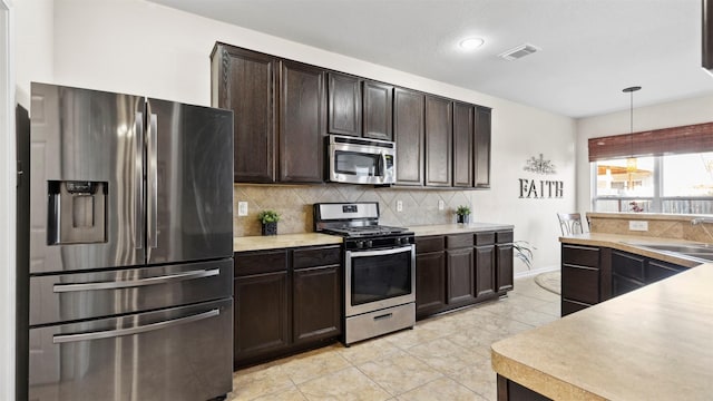 kitchen with appliances with stainless steel finishes, backsplash, dark brown cabinets, sink, and decorative light fixtures