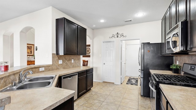 kitchen with kitchen peninsula, appliances with stainless steel finishes, backsplash, sink, and light tile patterned floors