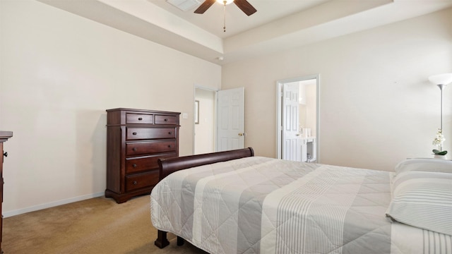 bedroom featuring ceiling fan, ensuite bathroom, light carpet, and a tray ceiling