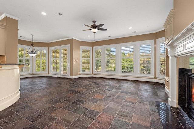 unfurnished living room with a tiled fireplace, ceiling fan, plenty of natural light, and ornamental molding