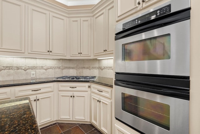 kitchen featuring backsplash, cream cabinets, dark stone countertops, dark tile patterned floors, and appliances with stainless steel finishes