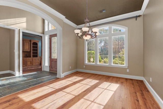 unfurnished dining area featuring crown molding, wood-type flooring, and an inviting chandelier