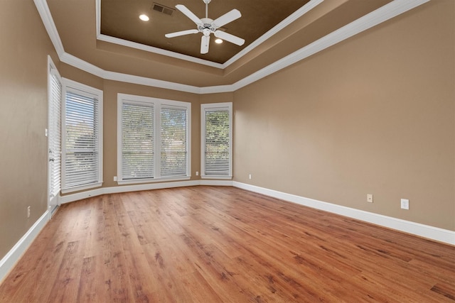 empty room featuring light wood-type flooring, a raised ceiling, ceiling fan, and ornamental molding