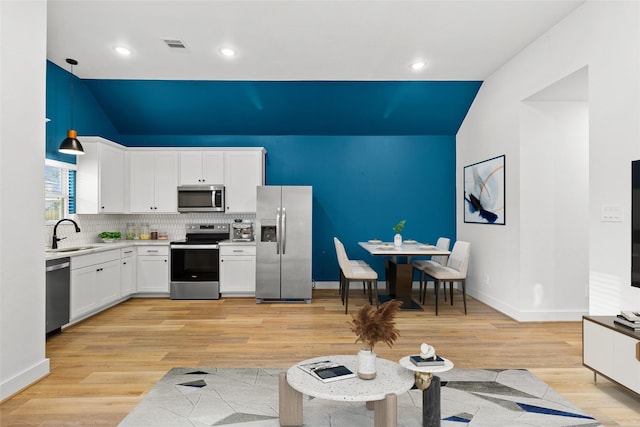 kitchen with pendant lighting, sink, white cabinetry, stainless steel appliances, and light hardwood / wood-style floors