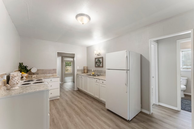 kitchen with white refrigerator, sink, light stone countertops, light hardwood / wood-style floors, and white cabinetry