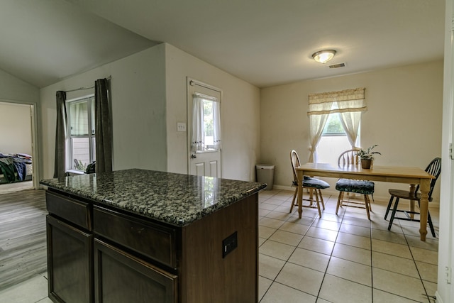 kitchen featuring plenty of natural light, light tile patterned flooring, dark stone counters, and dark brown cabinets