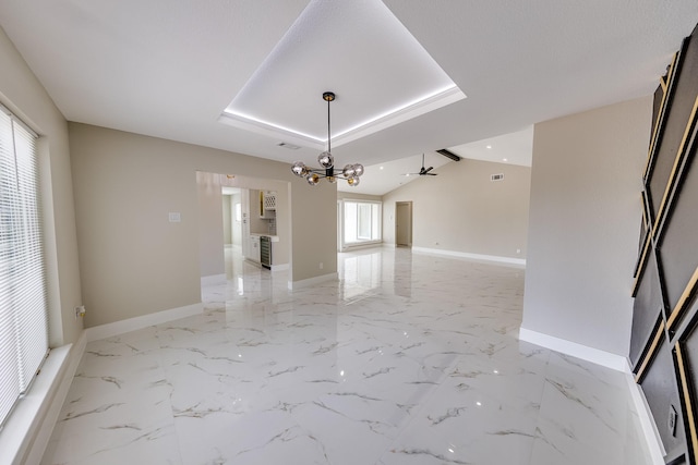 unfurnished room with ceiling fan with notable chandelier and a tray ceiling