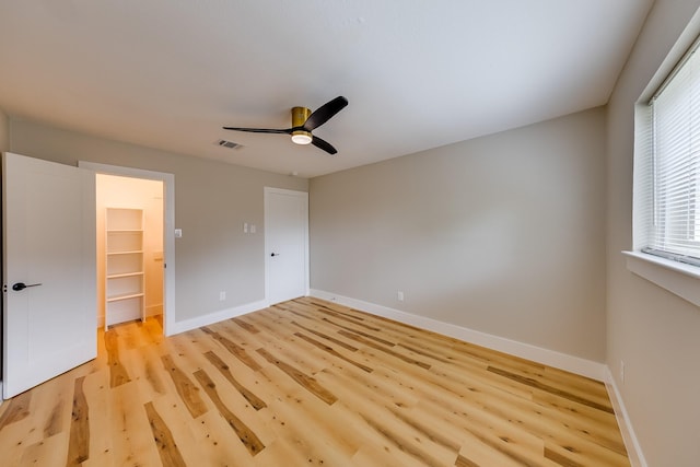 unfurnished bedroom with a walk in closet, ceiling fan, a closet, and light hardwood / wood-style floors