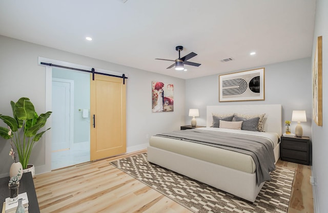 bedroom featuring hardwood / wood-style floors, ceiling fan, a barn door, and connected bathroom