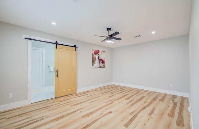 empty room with a barn door, ceiling fan, and light wood-type flooring