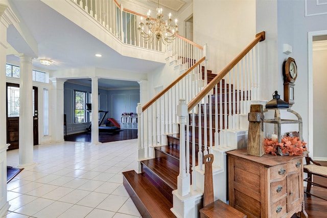 stairway with tile patterned flooring, a notable chandelier, decorative columns, crown molding, and a towering ceiling