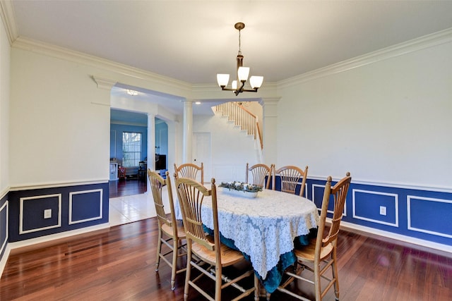 dining space featuring dark hardwood / wood-style flooring, ornate columns, crown molding, and an inviting chandelier