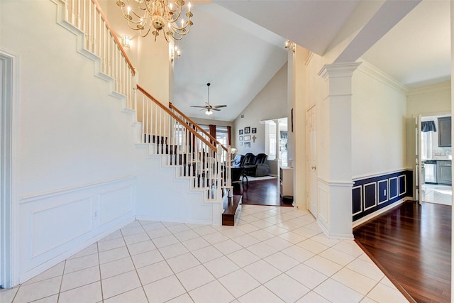 foyer entrance with light wood-type flooring, ornate columns, ornamental molding, ceiling fan with notable chandelier, and high vaulted ceiling